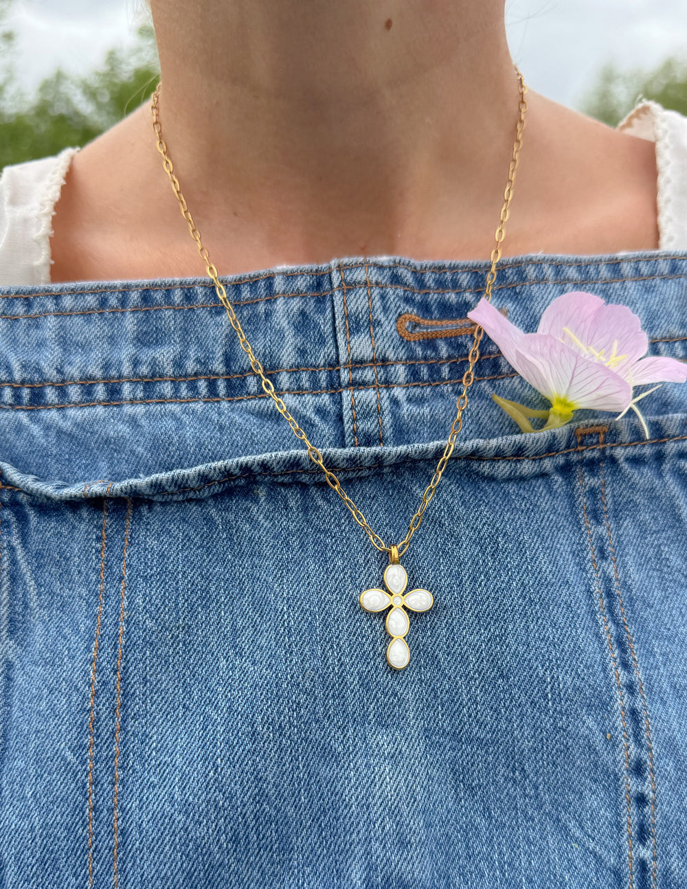 Close-up of white-detailed cross pendant on a gold-tone paperclip chain