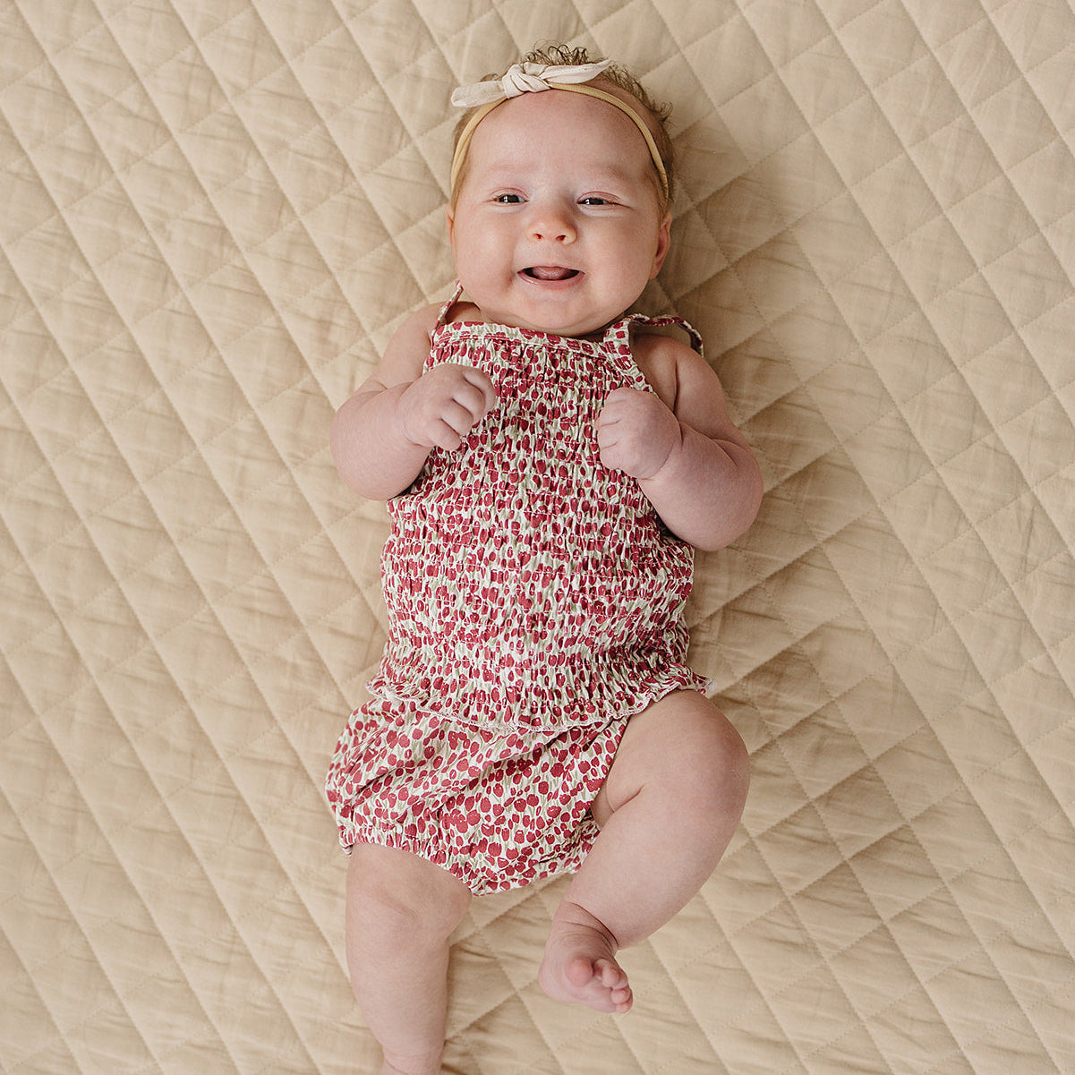 Baby in a floral romper lying on a textured beige surface