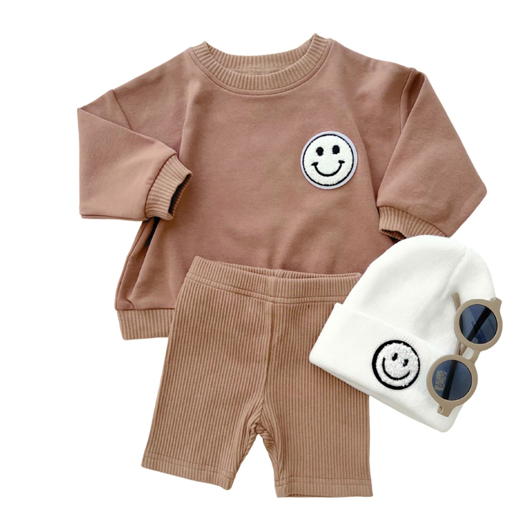 Children's brown outfit with smiley face design, white beanie, and sunglasses on a white background