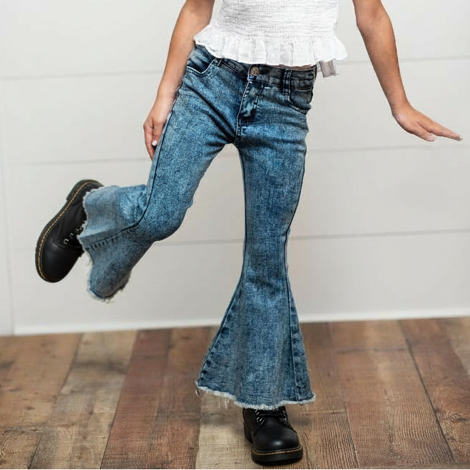 Child wearing a white top and blue jeans with a wooden floor and white wall background