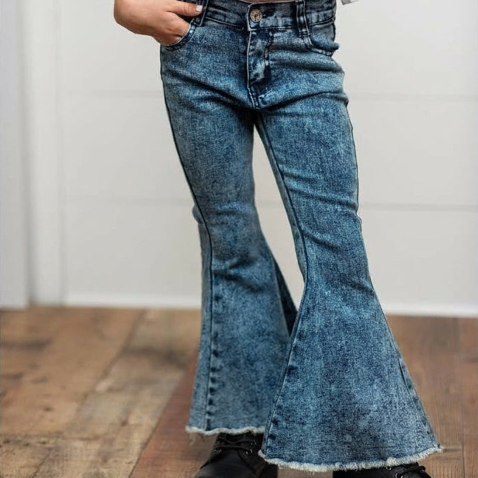 Person wearing a white blouse with ruffled sleeves and blue flared jeans on a wooden floor.