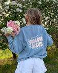 Model holding flowers while wearing the Bluebell Follow Jesus crewneck with pastel lettering on the back
