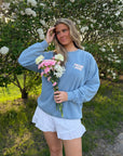 Model wearing the Bluebell Follow Jesus Unisex Crewneck with light-colored shorts and holding a bouquet
