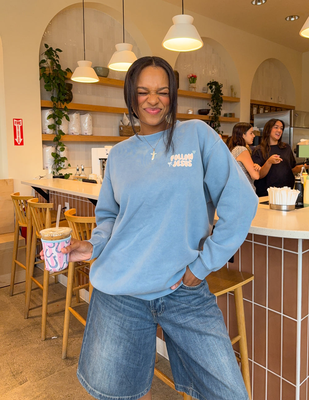 Model wearing the Bluebell Follow Jesus crewneck with jeans inside a café