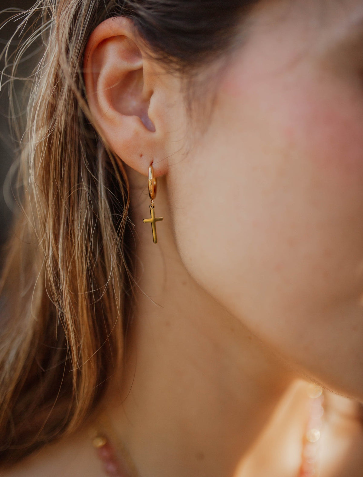 Side view of a model wearing a gold-plated hoop earring with a delicate dangling cross