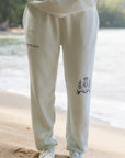 Person wearing a light-colored tracksuit with logos on the beach