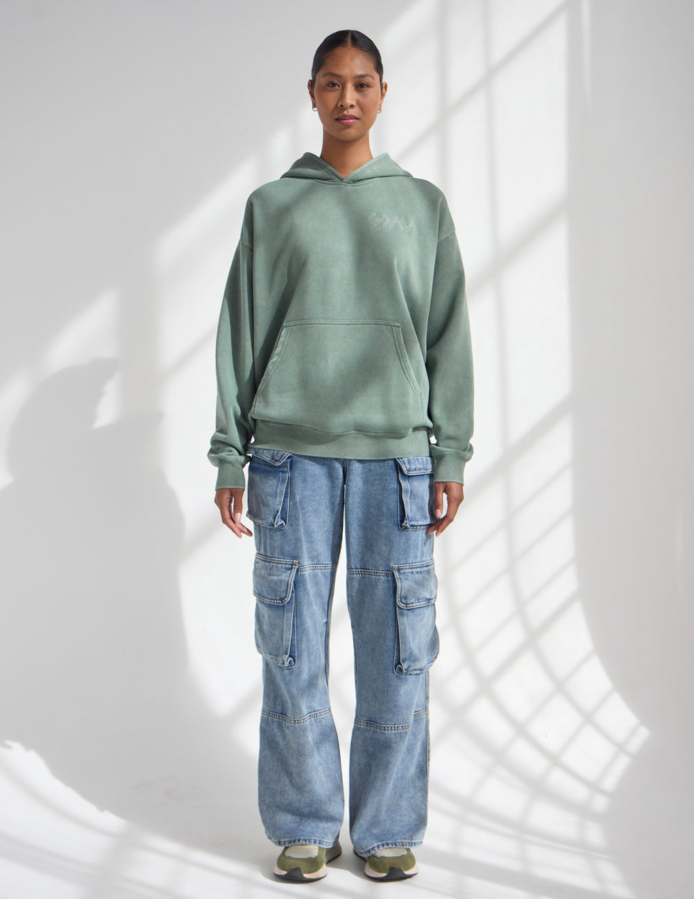 Front view of the relaxed moss green God Is Greater Hoodie worn with blue jeans.
