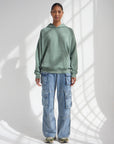 Front view of the relaxed moss green God Is Greater Hoodie worn with blue jeans.