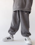 Child wearing Grey Mist God of Miracles sweatpants with elastic cuffs and white sneakers