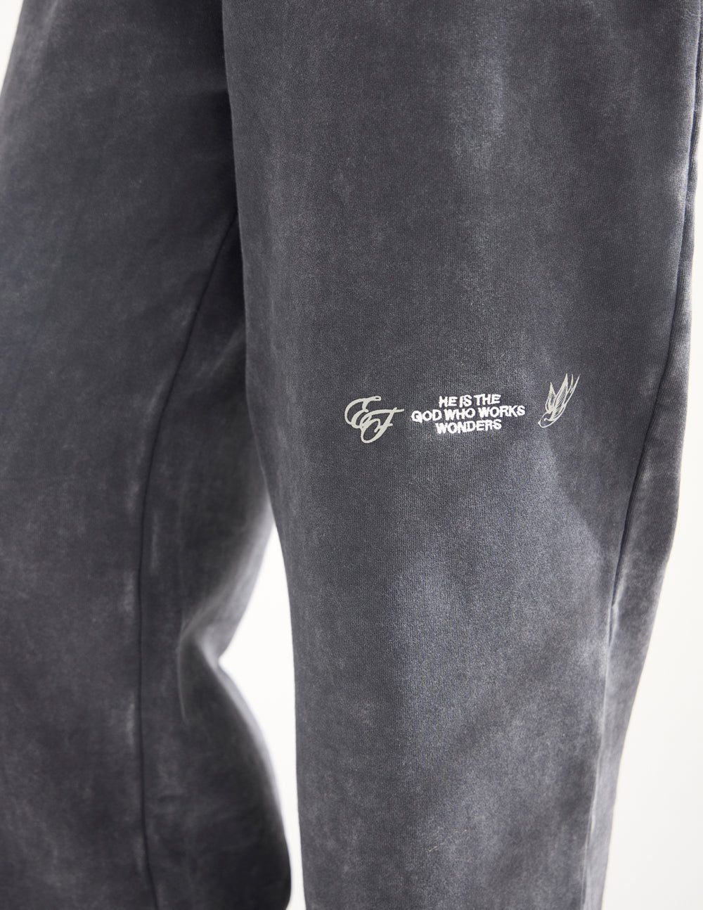 Close-up of light-colored embroidery on the black God of Miracles sweatpants.