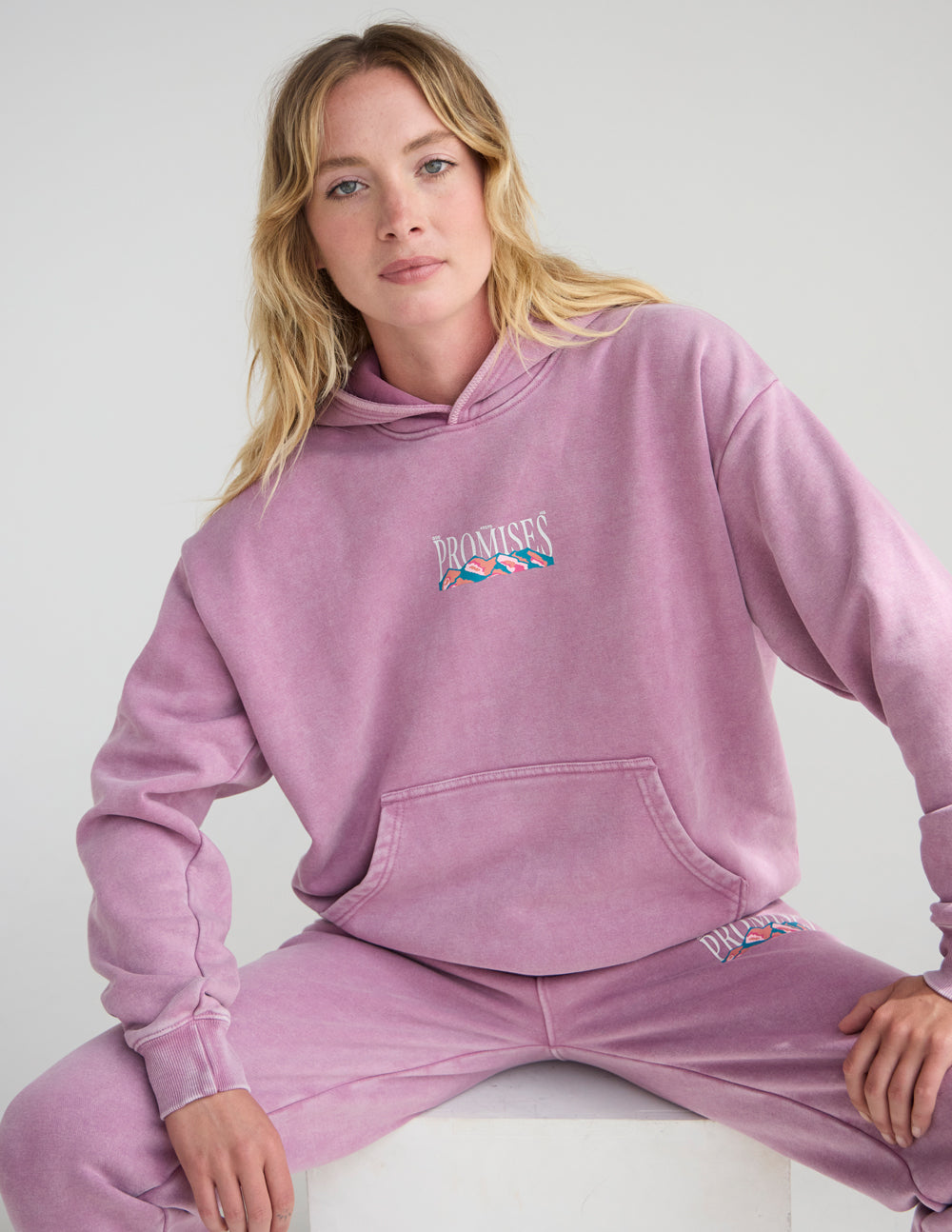 Woman seated in the Bordeaux God’s Promises Hoodie, showing the front graphic and relaxed fit.