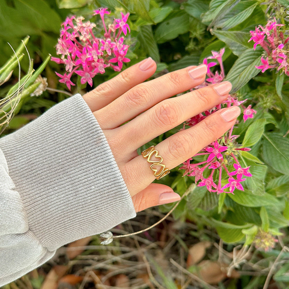 Hand with a gold ring touching pink flowers among green leaves