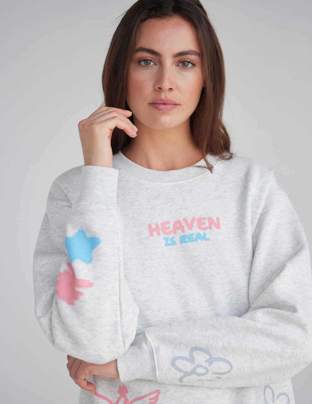 Heaven Is Real chest lettering and colorful sleeve graphics on a heather grey crewneck sweatshirt