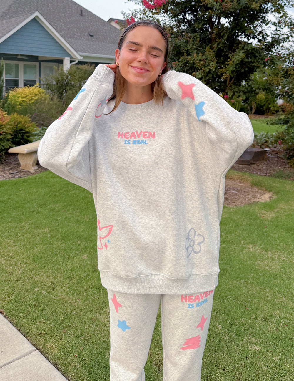 Model wearing the Heaven Is Real heather grey sweatshirt with coordinating sweatpants outdoors