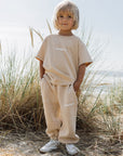 Child standing outdoors in the oversized Nomad Heaven Kids Tee with coordinating neutral pants.