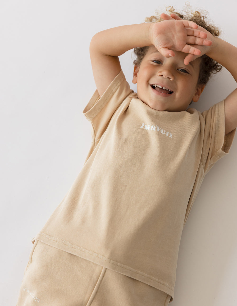 Child wearing the Nomad Heaven Kids Tee with arms raised against a light studio background.
