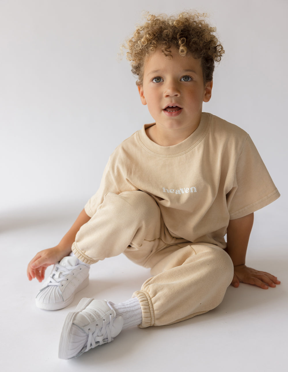 Child sitting on the floor wearing the oversized Heaven Kids Tee with coordinating pants.