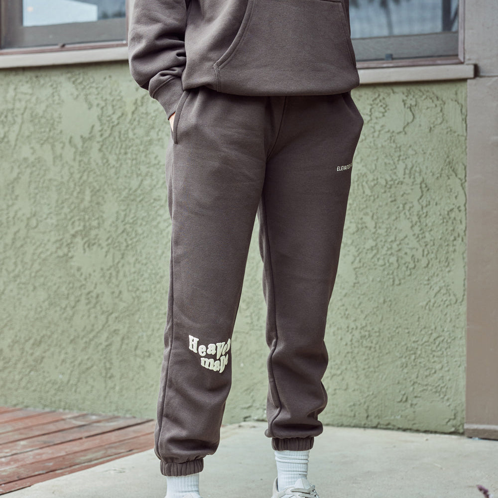 Person wearing a brown tracksuit with white text standing against a green wall.