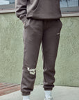 Person wearing a brown tracksuit with white text standing against a green wall.
