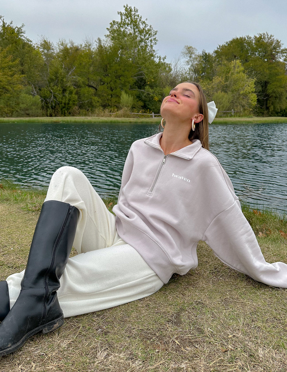 Model seated beside a lake wearing the Grey Lilac Heaven pullover with light-colored pants