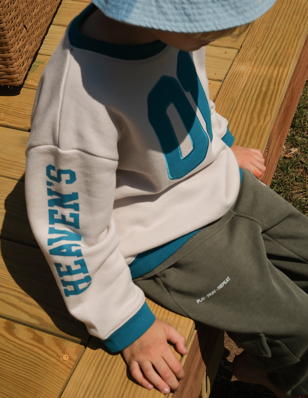 Close-up of teal Heaven’s Favorite sleeve lettering on a Pumice Stone kids sweatshirt