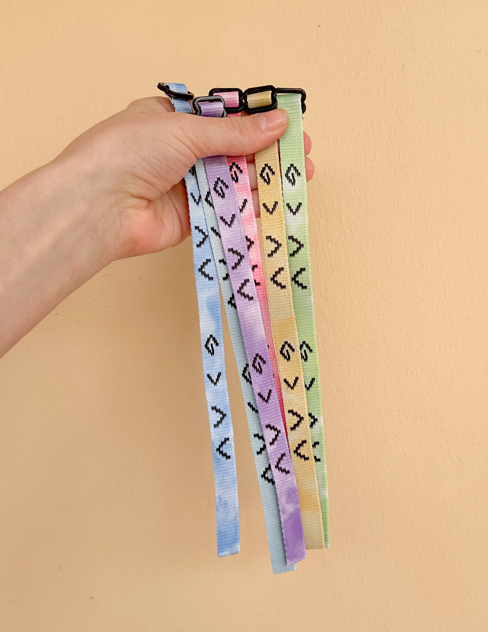 Hand holding six adjustable tie-dye bracelets with God is greater than the highs and lows symbols