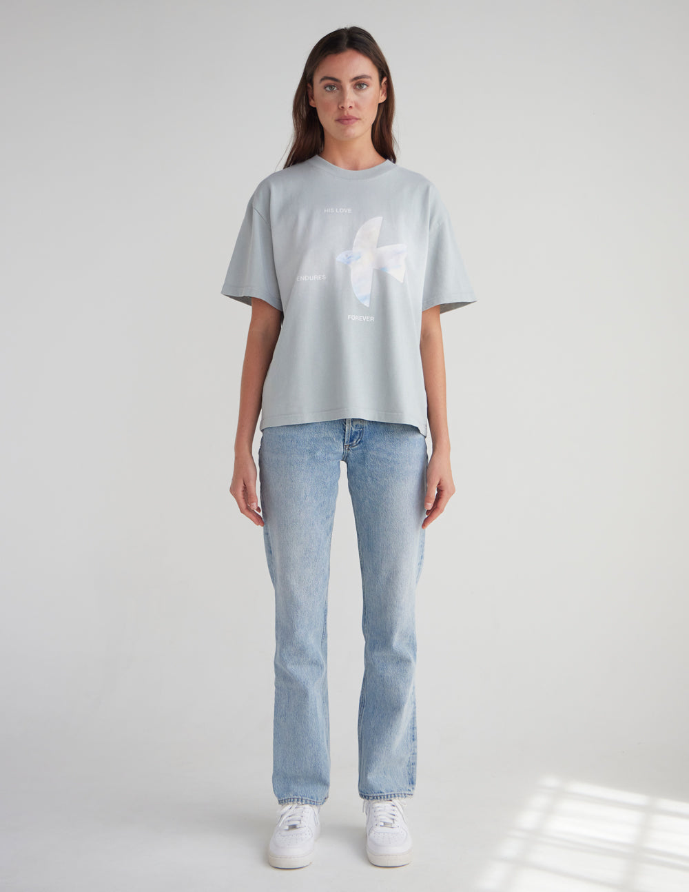 Full-length view of the His Love Endures Forever tee styled with jeans and white sneakers