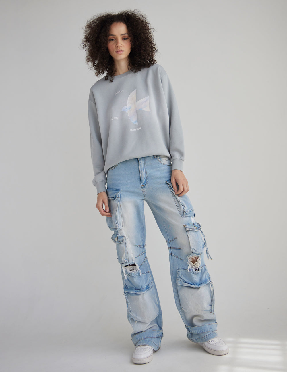 Full-length view of a woman wearing the Pearl Blue crewneck sweatshirt with distressed jeans