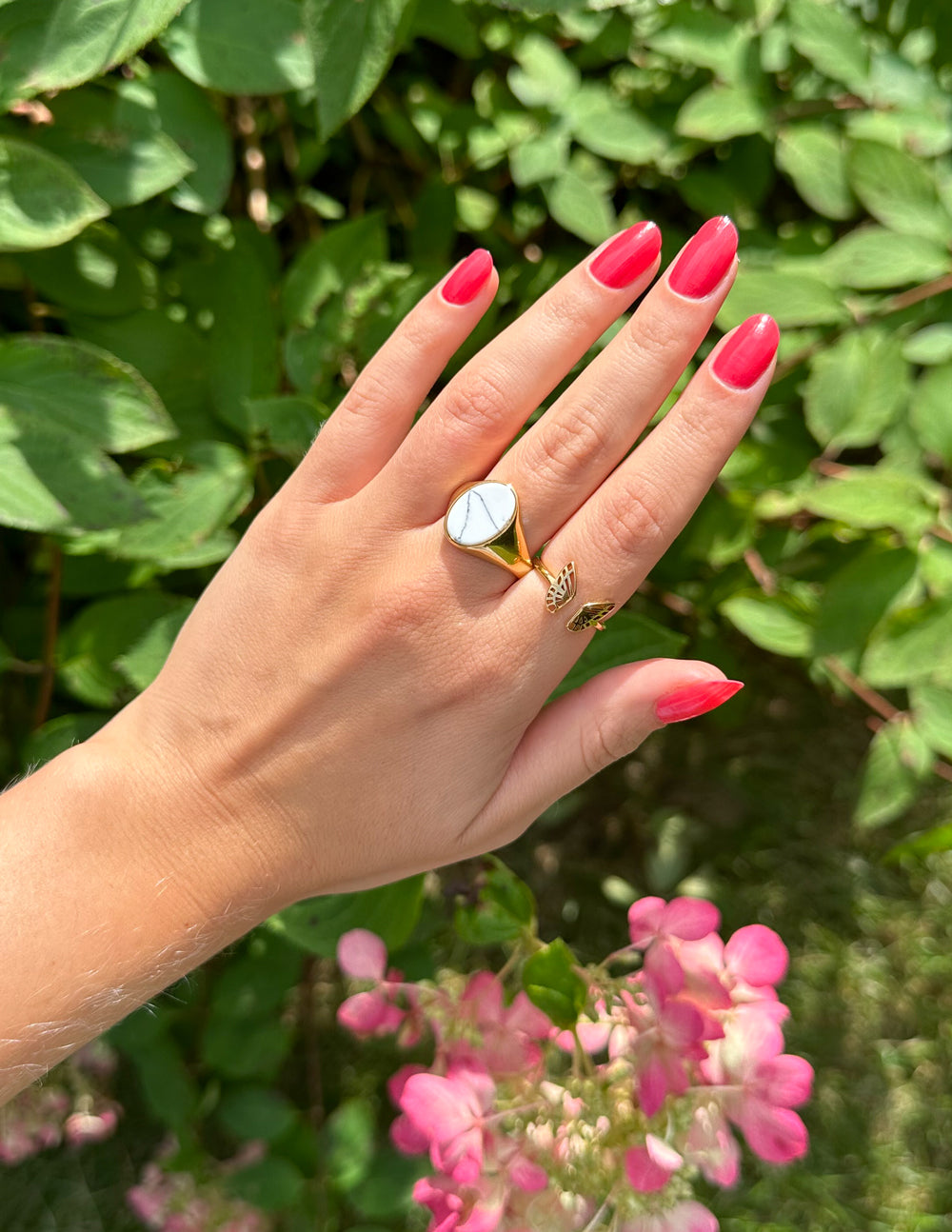 Howlite Stone Gold-Tone Ring worn on a hand with bright pink nails beside green foliage and pink flowers