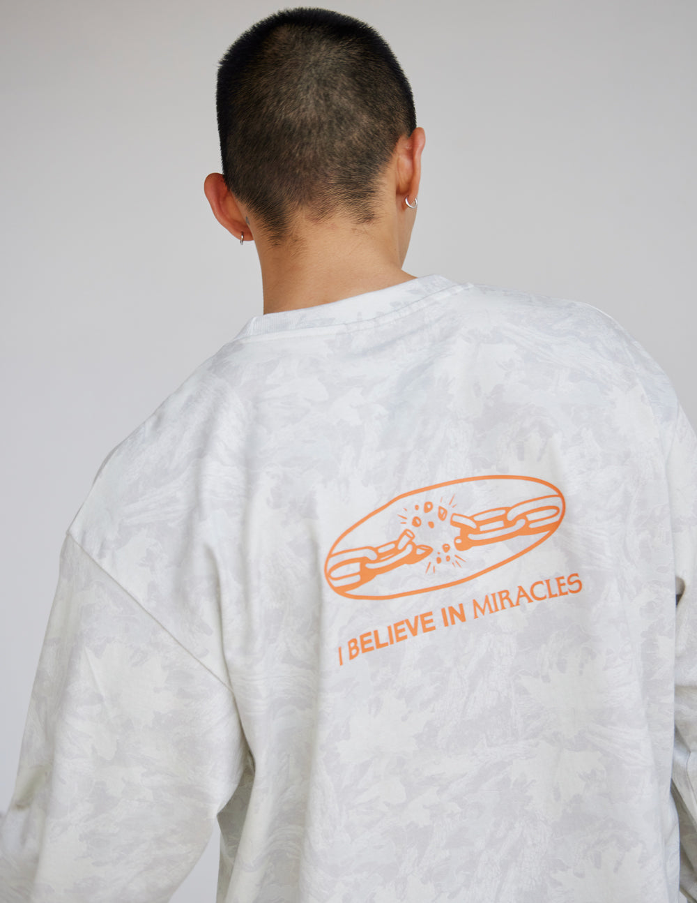Close-up of the orange back graphic on the I Believe in Miracles White Camo tee