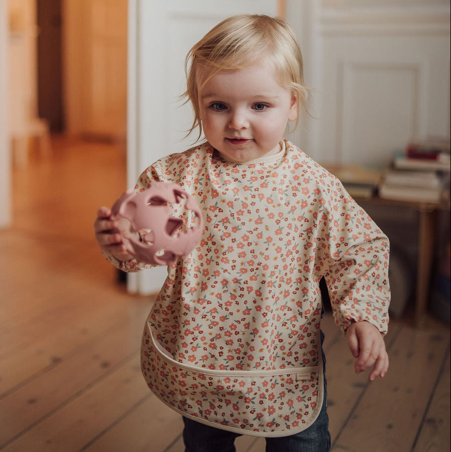 Child holding a pink toy in a room with wooden floors and white walls.