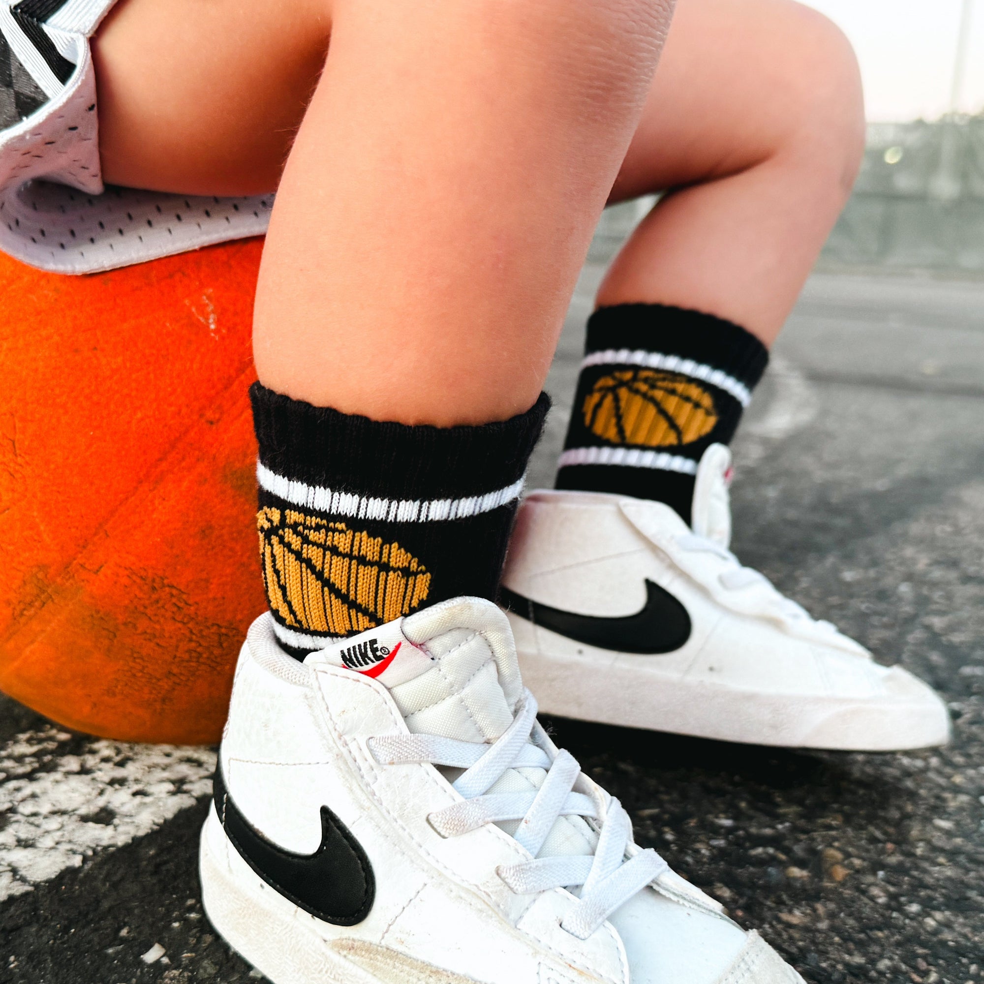 Person wearing white sneakers with black Nike logo, black socks with gold accents, and sitting on a rock.