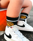 Person wearing white sneakers with black Nike logo, black socks with gold accents, and sitting on a rock.