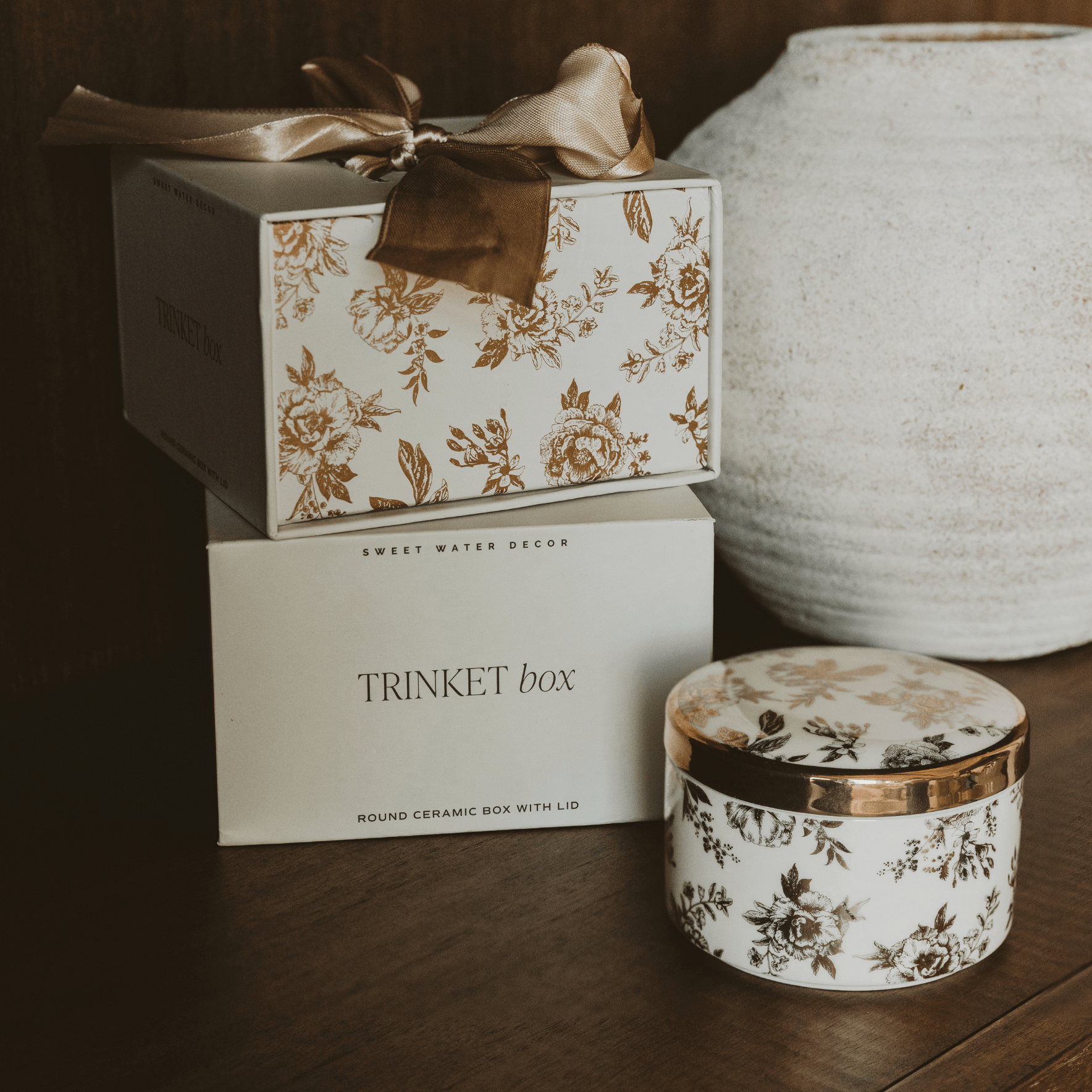 Decorative trinket box with floral design and ribbon, next to a ceramic container on a wooden surface.