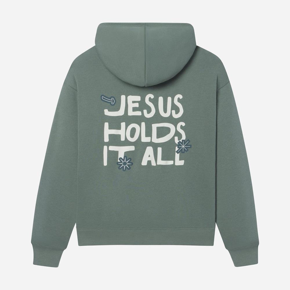 Green hoodie with 'Jesus Holds It All' text on the back against a light gray background