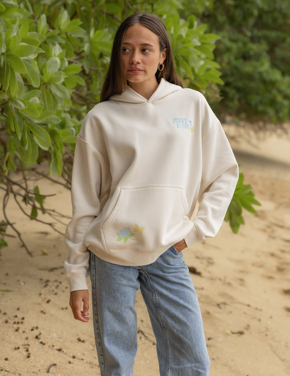 Model wearing the relaxed-fit Jesus Is Alive hoodie in Nimbus Cloud with jeans outdoors