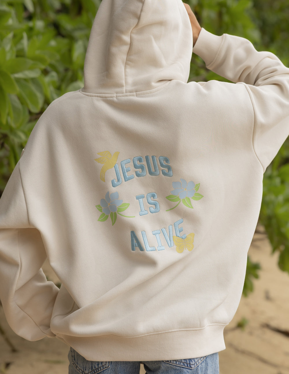 Back detail of the Nimbus Cloud Jesus Is Alive hoodie with blue lettering and pastel flowers
