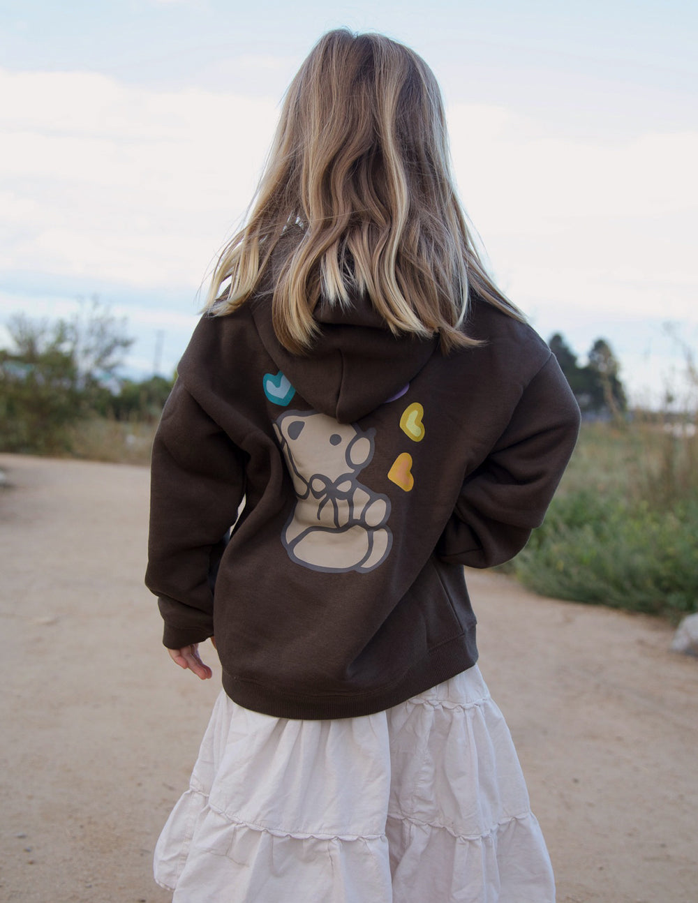 Back view of a child wearing the Coffee Jesus Loves You Kids Hoodie with a light-colored skirt outdoors