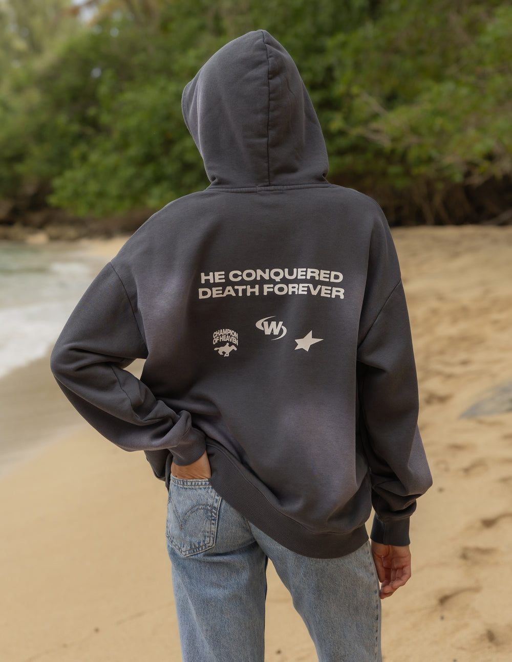 Model wearing the Black Tide Jesus Wins Hoodie with the hood up and back message visible outdoors