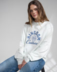 Woman seated in the Kingdom Culture long sleeve tee with blue lettering, styled with jeans.