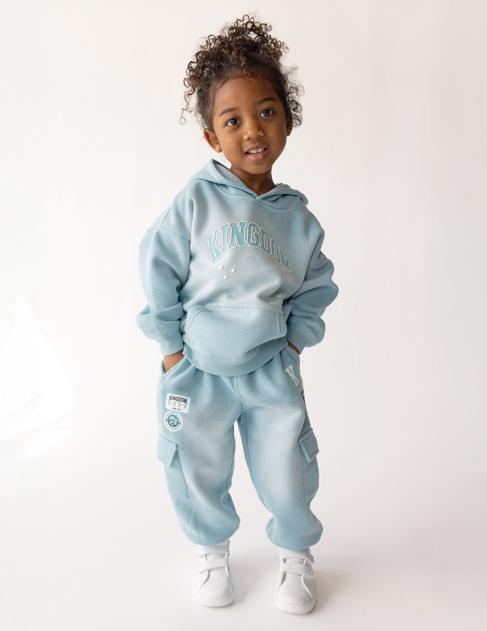 Child modeling the Air Blue Kingdom Kids Hoodie with coordinating pants and white sneakers