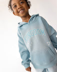 Child smiling while wearing the Air Blue Kingdom Kids Hoodie with a front kangaroo pocket