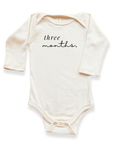 Cream organic cotton long sleeve baby bodysuit with three months lettering.