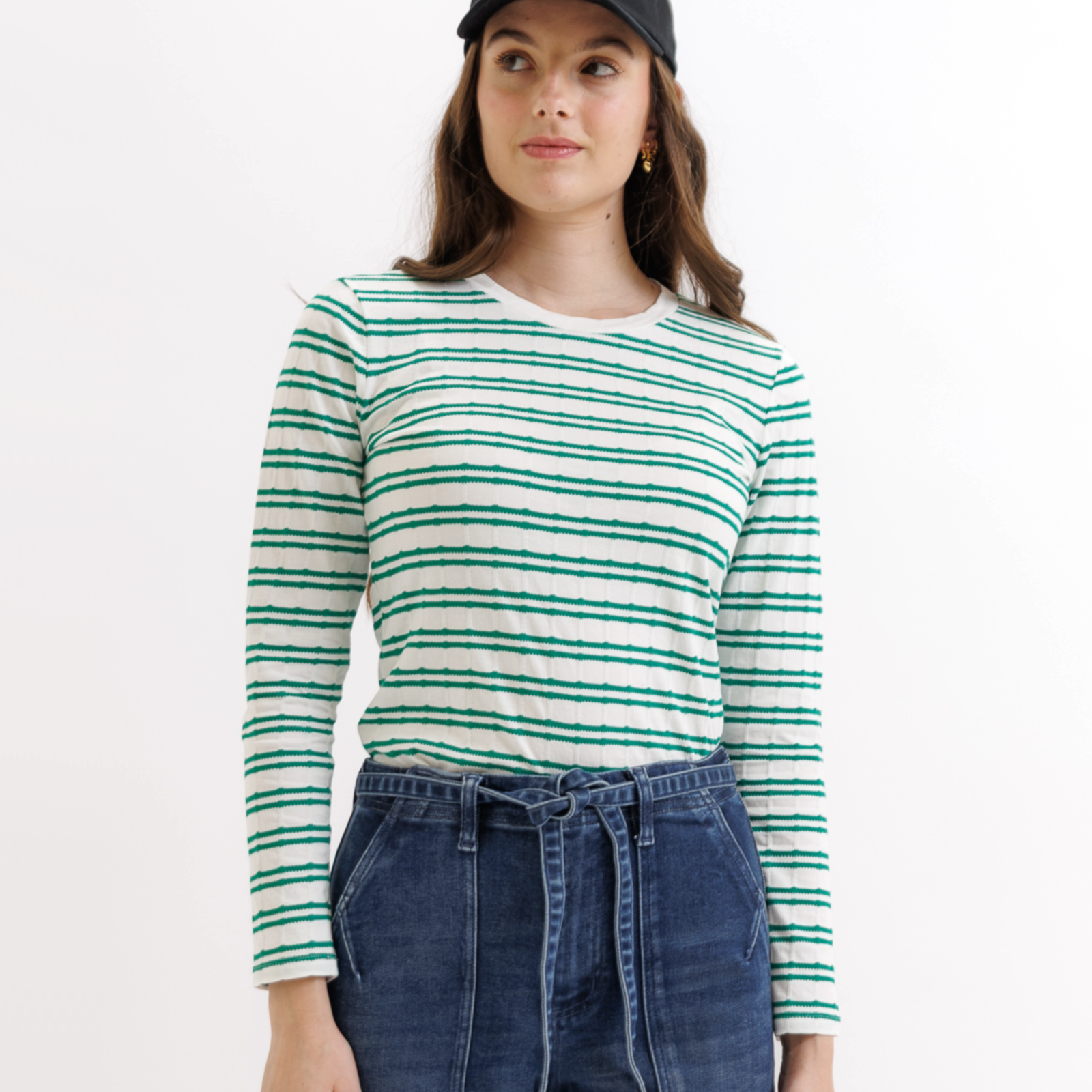 Woman wearing a green and white striped long-sleeve shirt and blue jeans on a white background