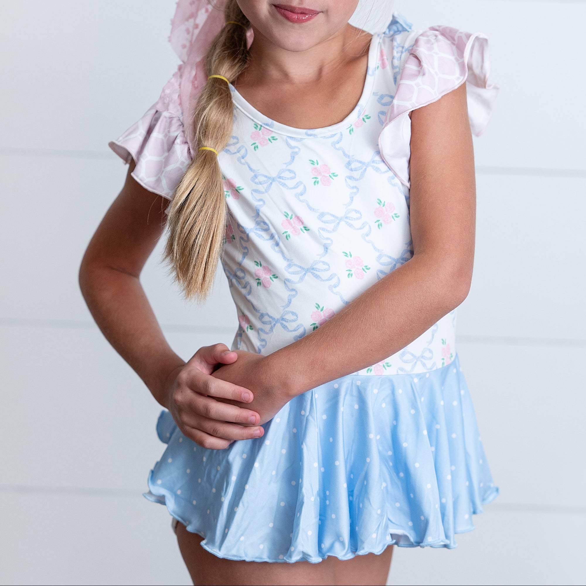 Young girl wearing a light blue dress with pink sleeves against a white background