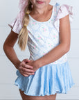 Young girl wearing a light blue dress with pink sleeves against a white background