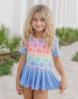 Young girl wearing a colorful checkered dress with a floral pattern on a garden path.