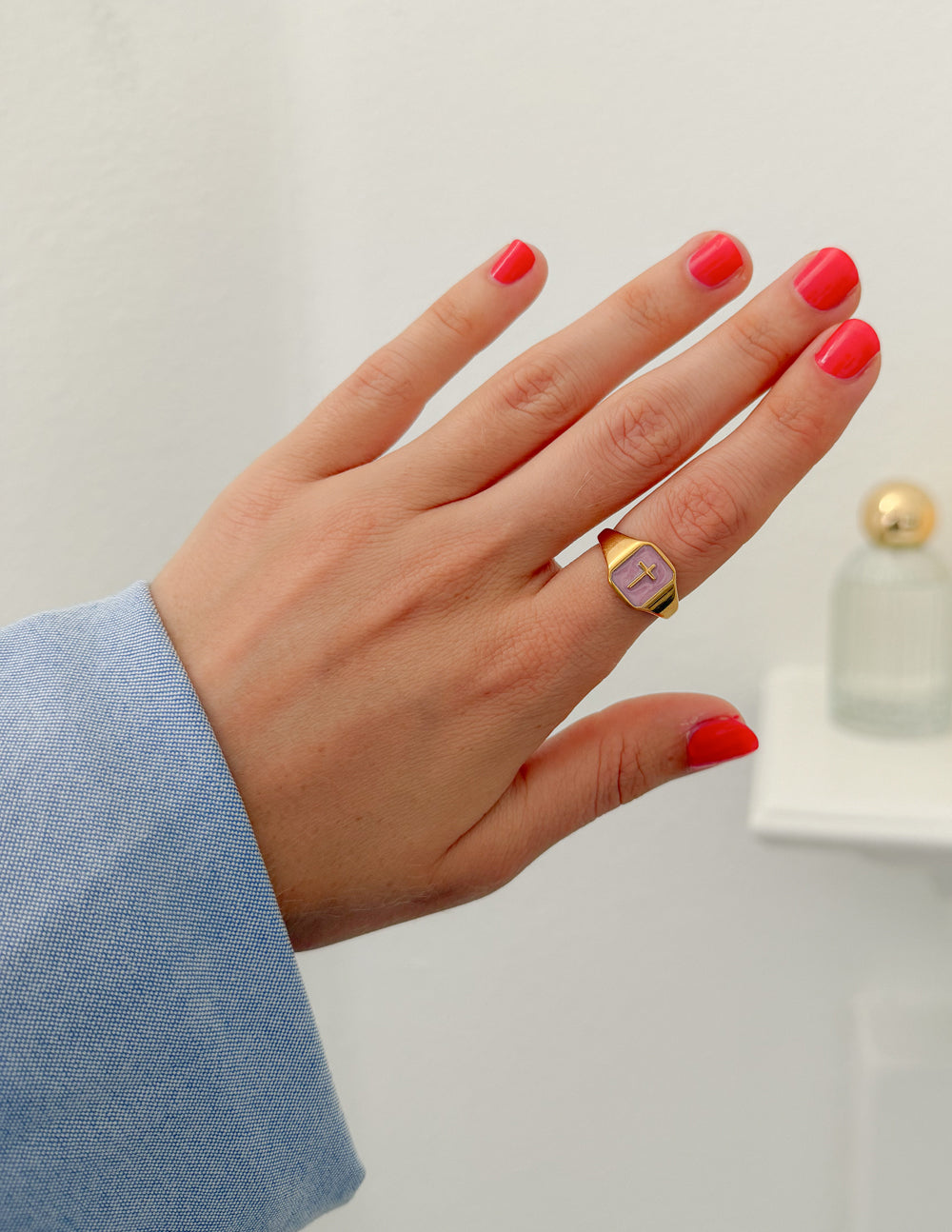 Lilac Enamel Cross Ring worn on a hand with pink nails and a blue sleeve indoors