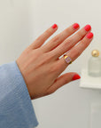Lilac Enamel Cross Ring worn on a hand with pink nails and a blue sleeve indoors