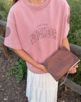 Close-up of the Ash Rose Love Your Neighbor tee showing front lettering above a Bible held by the model